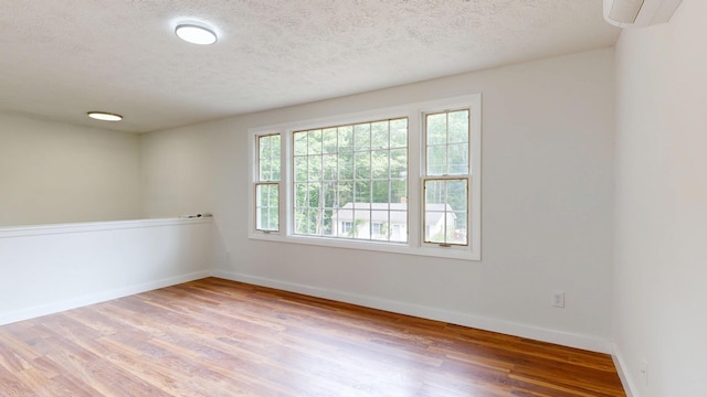 1 Barker St, Jay, ME 04239 - empty room with wood finished floors, a textured ceiling, a wall mounted air conditioner, and baseboards