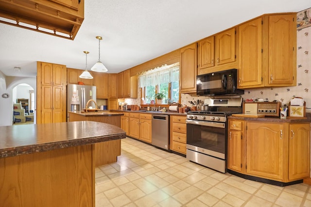 426 Fuller Rd, Carmel, ME 04419 - kitchen featuring stainless steel appliances, dark countertops, a center island with sink, arched walkways, and hanging light fixtures