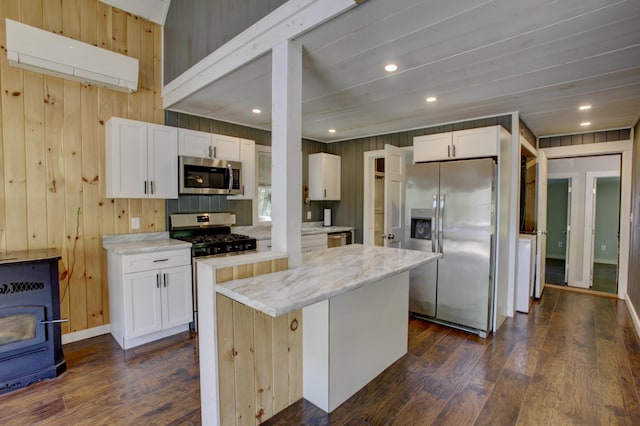 6 Meadow Ln, Sabattus, ME 04280 - kitchen featuring stainless steel appliances, a kitchen island, a wood stove, dark wood finished floors, and wood walls