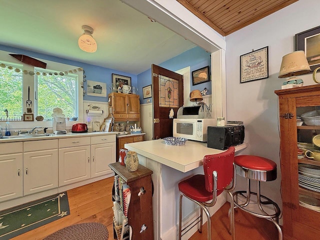 99 Huddle Rd, Bristol, ME 04554 - kitchen with white microwave, white cabinets, light wood-style flooring, black microwave, and a breakfast bar