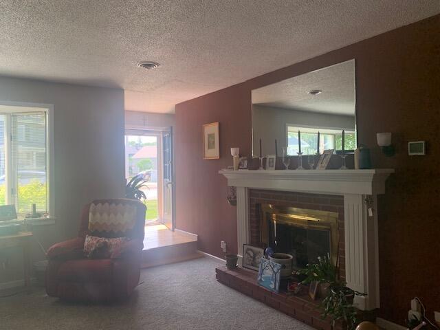 48 13th St, Bangor, ME 04401 - living area with a brick fireplace, a textured ceiling, carpet floors, and healthy amount of natural light