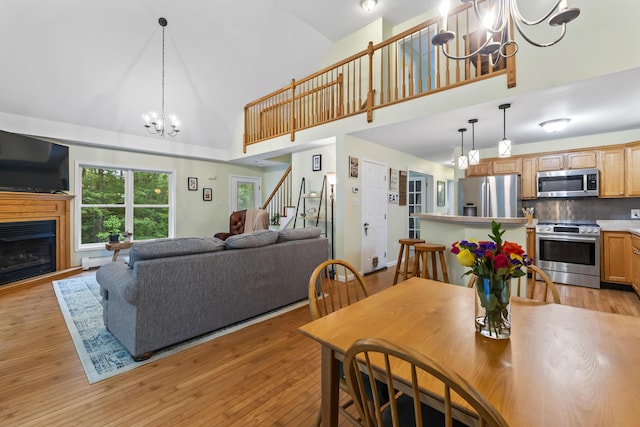 47 Double M Ln, Woolwich, ME 04579 - dining space featuring a chandelier, stairway, high vaulted ceiling, light wood-style floors, and a glass covered fireplace