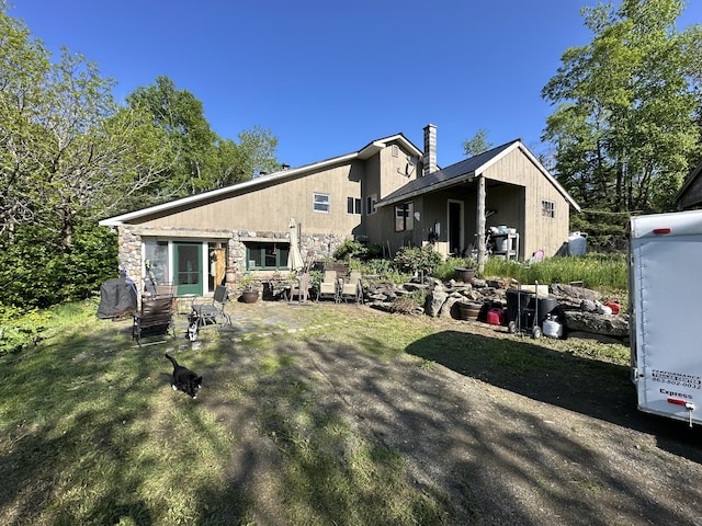 396 Smyrna Town Line Rd, Smyrna, ME 04780 - back of house featuring stone siding, a chimney, and a patio area