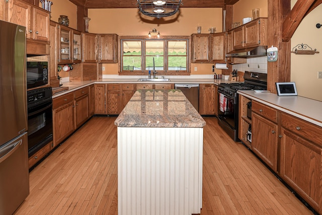 370 Center Conway Rd, Brownfield, ME 04010 - kitchen with black appliances, brown cabinetry, under cabinet range hood, a kitchen island, and light wood-style floors