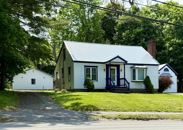 755 Main St, Calais, ME 04619 - view of front of house with a chimney, asphalt driveway, a front yard, a metal roof, and an outdoor structure