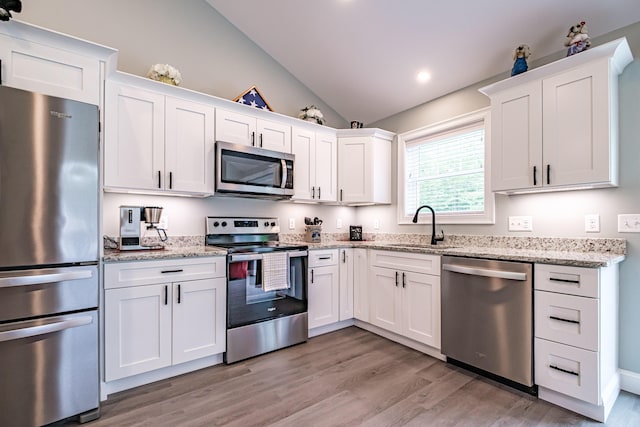 144 Ridley Rd, Sanford, ME 04073 - kitchen featuring appliances with stainless steel finishes, vaulted ceiling, white cabinetry, light wood finished floors, and light stone countertops