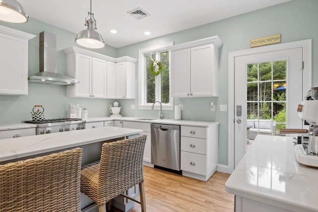 18 Frontier Way Unit 162, Arundel, ME 04046 - kitchen featuring stainless steel dishwasher, wall chimney range hood, white cabinetry, light wood-type flooring, and decorative light fixtures