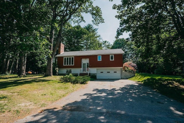 41 Curtis Ln, Milford, ME 04461 - bi-level home with asphalt driveway, a garage, a chimney, and a front lawn