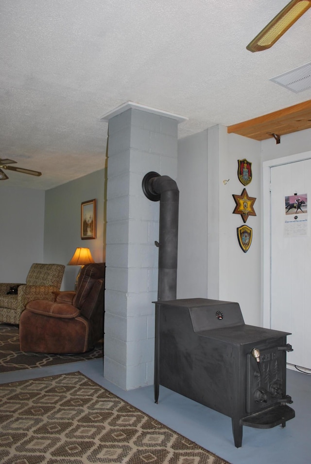 180 Chadbourne Rd, Harmony, ME 04942 - living room featuring a wood stove, a textured ceiling, ceiling fan, and concrete floors