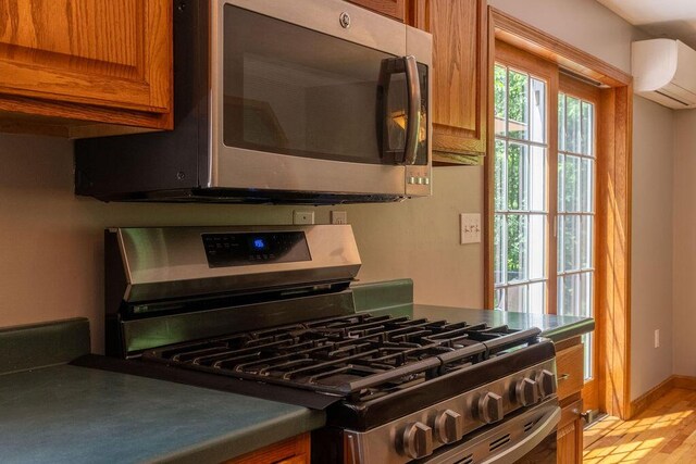 3350 Middle Rd, Sidney, ME 04330 - kitchen featuring stainless steel appliances, brown cabinets, an AC wall unit, light wood-type flooring, and dark countertops