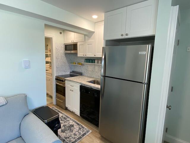 1072 Post Rd Unit 102, Wells, ME 04090 - kitchen featuring stainless steel appliances, white cabinets, light countertops, light wood-style floors, and decorative backsplash