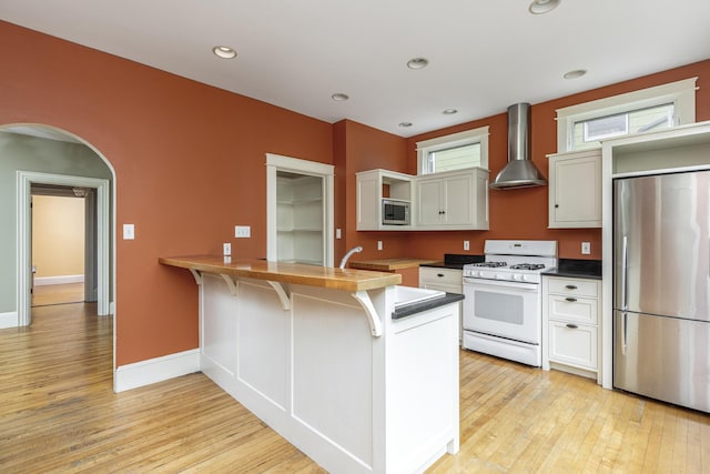 80 Melbourne St, Portland, ME 04101 - kitchen with appliances with stainless steel finishes, wall chimney range hood, open shelves, a peninsula, and light wood-style floors