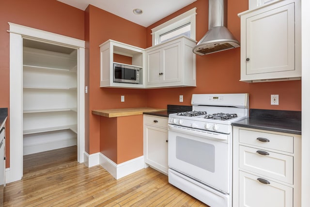 80 Melbourne St, Portland, ME 04101 - kitchen with white range with gas stovetop, wall chimney range hood, stainless steel microwave, light wood-style floors, and dark countertops