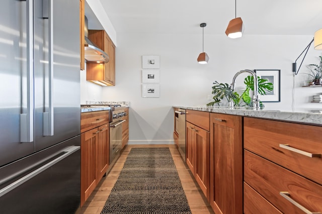 156 Sheridan St Unit 2A, Portland, ME 04101 - kitchen featuring high end appliances, brown cabinetry, wall chimney exhaust hood, light stone counters, and light wood finished floors