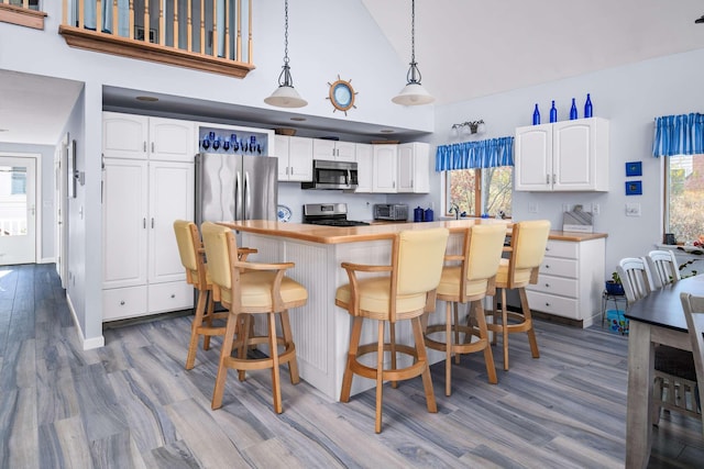 204 Nubble Rd, York, ME 03909 - kitchen with stainless steel appliances, wood finished floors, high vaulted ceiling, white cabinets, and healthy amount of natural light