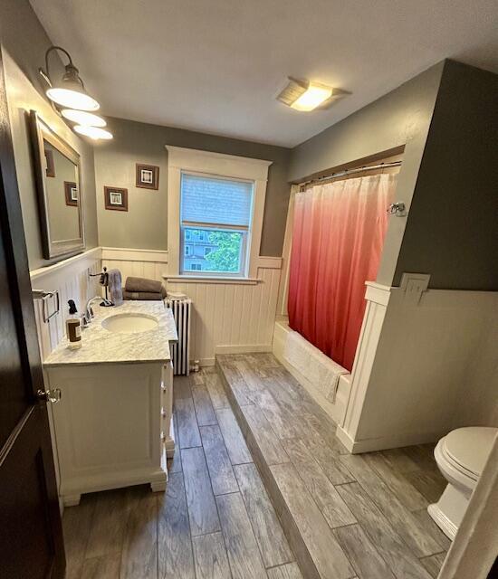 28 Holly St, Auburn, ME 04210 - full bathroom featuring wood finished floors, vanity, wainscoting, shower / bath combination with curtain, and radiator
