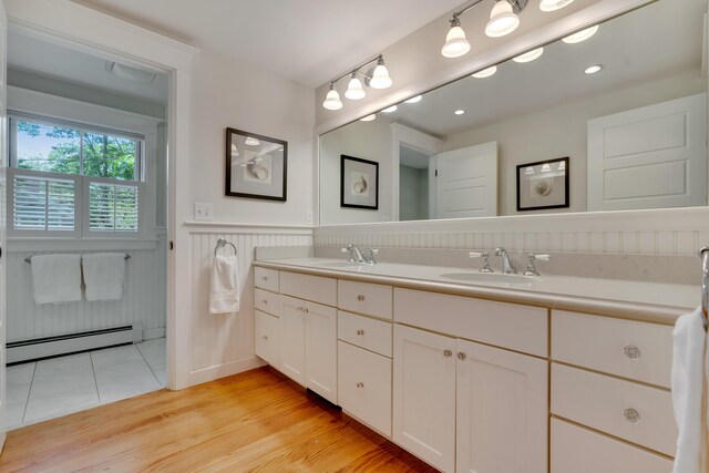 13 Norwood Ln, Kennebunkport, ME 04046 - bathroom featuring a baseboard radiator, double vanity, wainscoting, wood finished floors, and a decorative wall