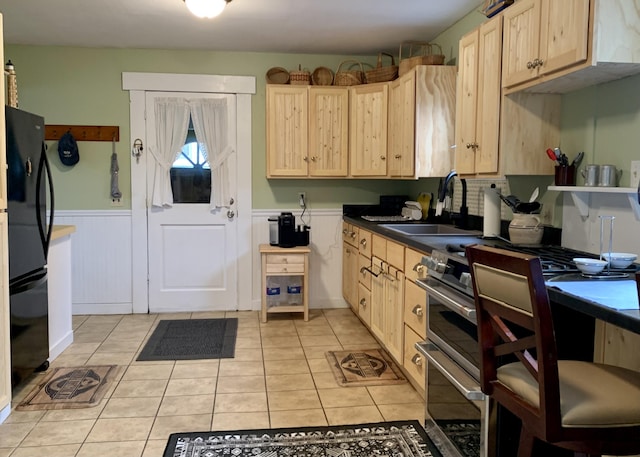 361 Water St, Addison, ME 04606 - kitchen featuring light brown cabinets, freestanding refrigerator, light tile patterned floors, a wainscoted wall, and dark countertops