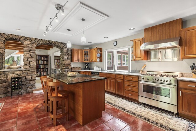 11 Everett Dow Dr, Woolwich, ME 04579 - kitchen with stainless steel appliances, wall chimney range hood, ornate columns, brown cabinetry, and dark stone counters
