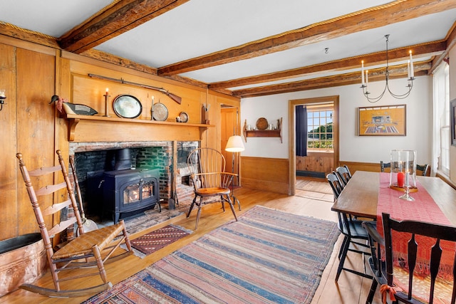 351 Mill Creek Rd, Islesboro, ME 04848 - dining area with a wood stove, light wood-style flooring, wooden walls, beamed ceiling, and wainscoting