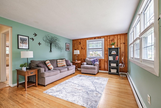 51 Burwell Ave, South Portland, ME 04106 - living room featuring a baseboard radiator, wood walls, light wood-type flooring, and a textured ceiling
