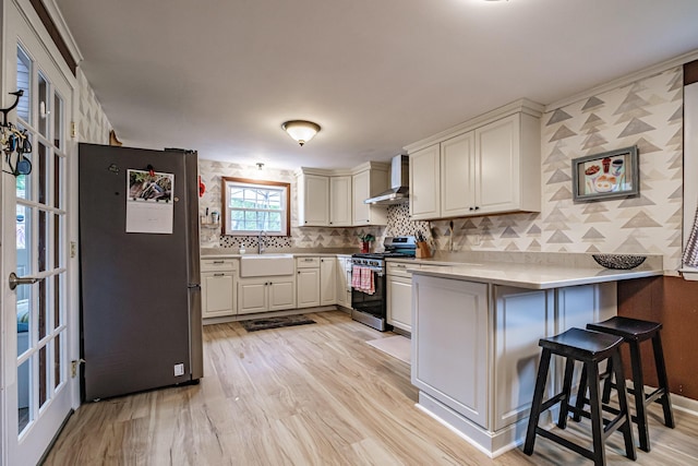 51 Burwell Ave, South Portland, ME 04106 - kitchen featuring appliances with stainless steel finishes, wall chimney range hood, a peninsula, light wood-style floors, and a breakfast bar