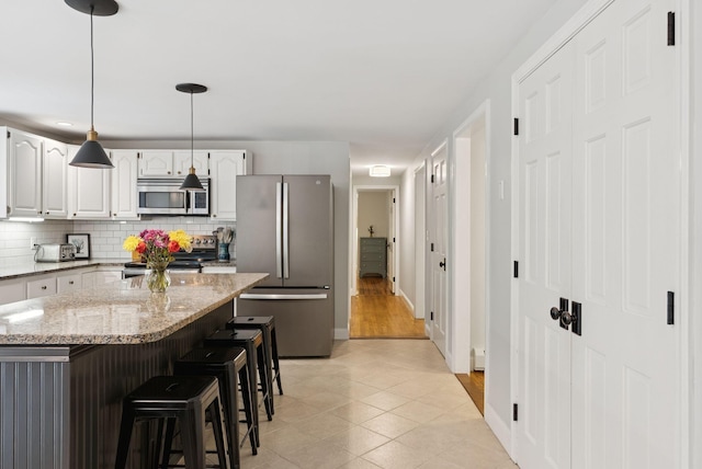 3 Flintlock Ln, Falmouth, ME 04105 - kitchen featuring appliances with stainless steel finishes, backsplash, a kitchen breakfast bar, light stone counters, and light tile patterned floors