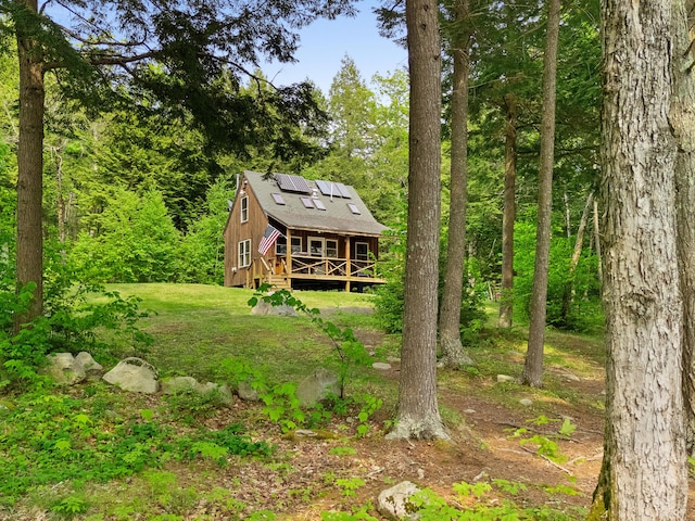 660 Sprague Rd, Waldoboro, ME 04572 - back of house with a wooden deck, roof mounted solar panels, a lawn, and a forest view
