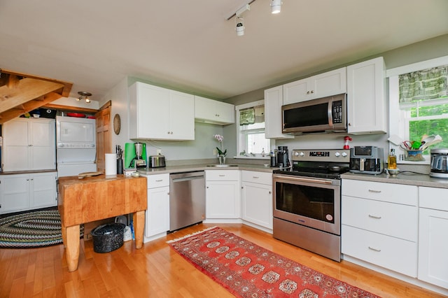 365 Waterville Rd, Skowhegan, ME 04976 - kitchen with appliances with stainless steel finishes, stacked washing machine and dryer, white cabinets, and light wood-style flooring