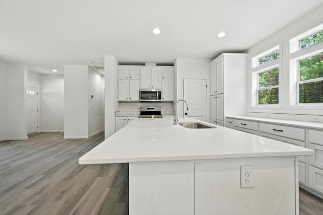 4 Willis Rd, Benton, ME 04901 - kitchen with appliances with stainless steel finishes, a kitchen island with sink, decorative backsplash, white cabinetry, and light wood finished floors