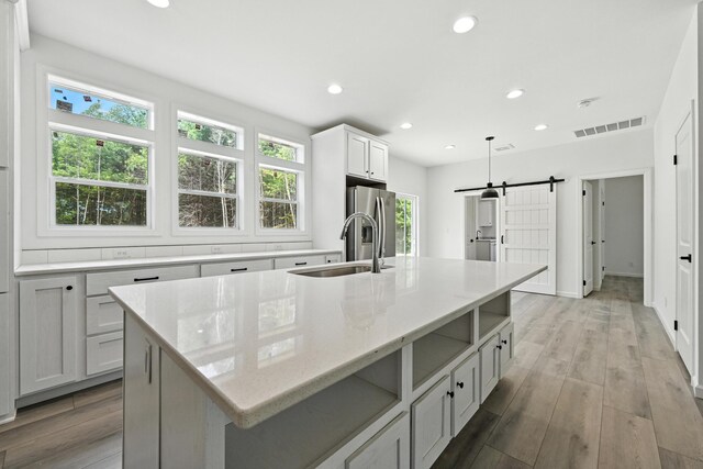 4 Willis Rd, Benton, ME 04901 - kitchen with a barn door, a center island with sink, recessed lighting, light wood-style floors, and stainless steel refrigerator with ice dispenser