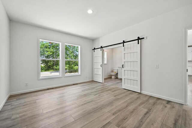 4 Willis Rd, Benton, ME 04901 - unfurnished bedroom with a barn door, light wood finished floors, connected bathroom, and recessed lighting