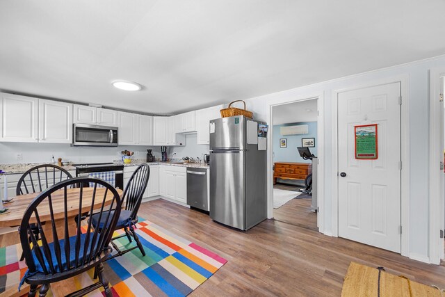 1165 Castine Rd, Penobscot, ME 04476 - kitchen with stainless steel appliances, a wall mounted air conditioner, light wood-type flooring, and white cabinetry