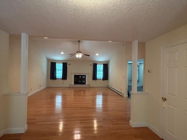 1 S Ridge Dr, Winslow, ME 04901 - unfurnished living room featuring a baseboard heating unit, ceiling fan, light wood-style flooring, a textured ceiling, and a glass covered fireplace