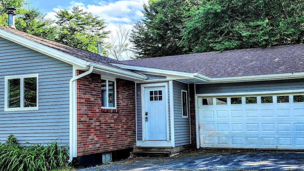 30 Grand Ave, Millinocket, ME 04462 - property entrance featuring an attached garage, roof with shingles, asphalt driveway, and brick siding