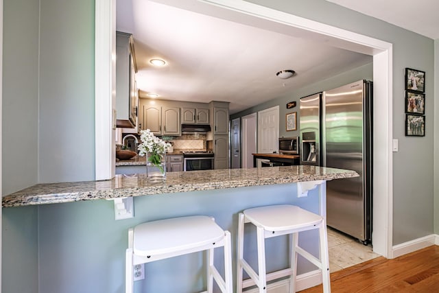 325 Ludlow St, Portland, ME 04102 - kitchen with appliances with stainless steel finishes, a peninsula, gray cabinetry, backsplash, and under cabinet range hood