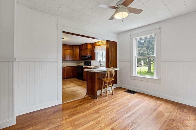 7 James St, Bingham, ME 04920 - kitchen featuring black electric range, light wood-type flooring, a peninsula, light countertops, and a wainscoted wall