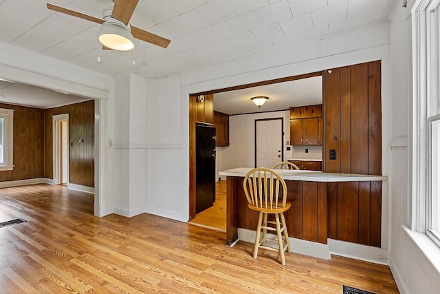 7 James St, Bingham, ME 04920 - kitchen with a ceiling fan, light countertops, light wood-style flooring, a breakfast bar area, and wood walls