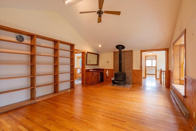 391 Main Rd, Islesboro, ME 04848 - unfurnished living room with lofted ceiling, a wood stove, light wood-style flooring, wainscoting, and a ceiling fan
