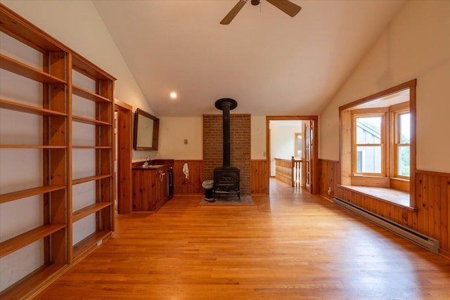 391 Main Rd, Islesboro, ME 04848 - unfurnished living room featuring a baseboard radiator, lofted ceiling, a wainscoted wall, a wood stove, and light wood finished floors