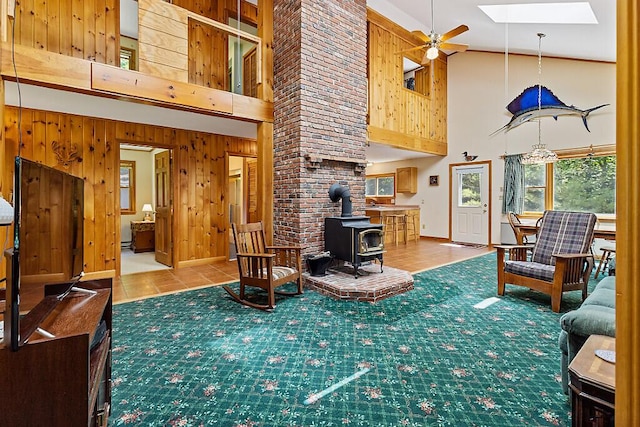 176 Perkins Beach Rd, Wayne, ME 04284 - living room with high vaulted ceiling, ceiling fan, wooden walls, a wood stove, and a skylight