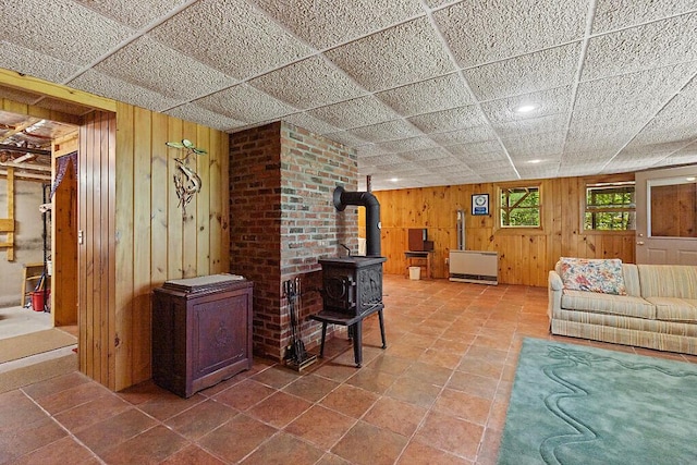 176 Perkins Beach Rd, Wayne, ME 04284 - living area featuring a wood stove, wood walls, radiator heating unit, tile patterned floors, and a paneled ceiling