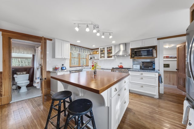 259 Mountain St, Camden, ME 04843 - kitchen featuring wall chimney range hood, appliances with stainless steel finishes, hardwood / wood-style flooring, white cabinetry, and butcher block countertops