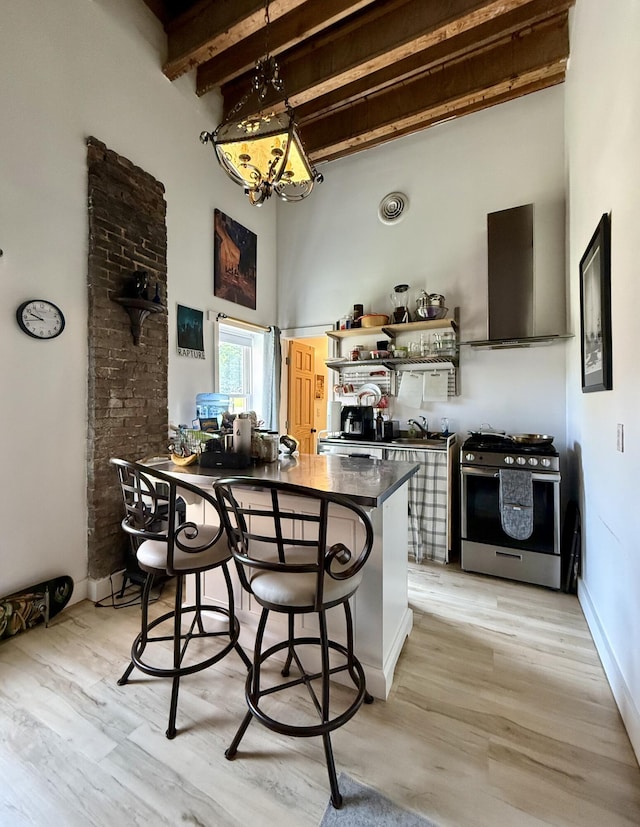 339 Main St, Calais, ME 04619 - kitchen with stainless steel range with gas stovetop, wall chimney exhaust hood, dark countertops, beam ceiling, and a kitchen breakfast bar
