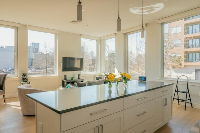 167 Newbury St Unit 206, Portland, ME 04101 - kitchen featuring light wood-style flooring, white cabinets, pendant lighting, open floor plan, and a center island
