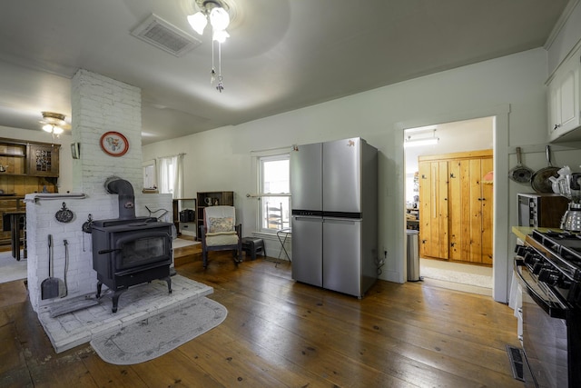878 State Route 32, Bristol, ME 04564 - kitchen with stainless steel appliances, a ceiling fan, a wood stove, white cabinets, and hardwood / wood-style floors