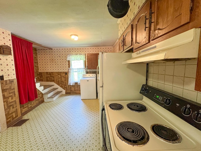 144 Main Rd, Burlington, ME 04417 - kitchen with electric stove, washer / dryer, under cabinet range hood, wallpapered walls, and brown cabinets