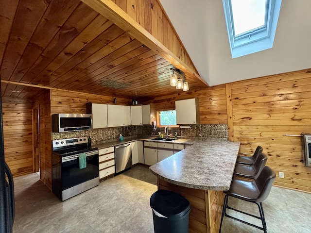 24 N Tiery St, Old Town, ME 04468 - kitchen featuring stainless steel appliances, a peninsula, wood walls, a skylight, and a breakfast bar
