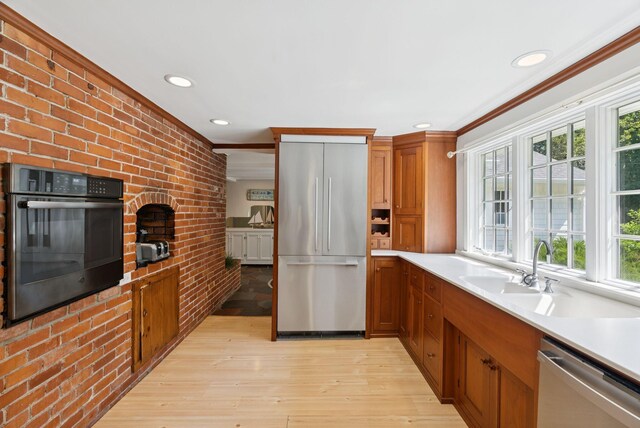 53 Beach Ave, Kennebunk, ME 04043 - kitchen with stainless steel appliances, brick wall, crown molding, light wood-type flooring, and brown cabinetry