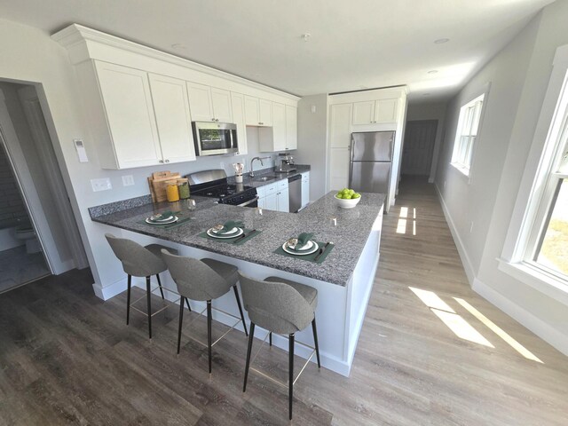106 Cumberland Ave Unit 201, Portland, ME 04101 - kitchen featuring stainless steel appliances, a peninsula, dark stone counters, light wood finished floors, and white cabinetry